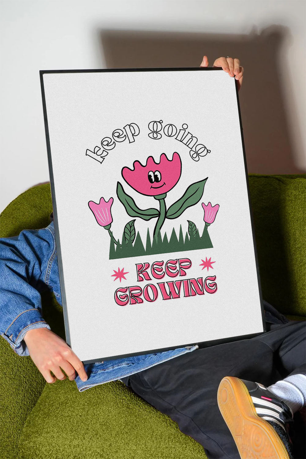 Siyah çerçeveli, beyaz zeminde pembe gülen çiçek, küçük çiçekler ve çimenler ile 'Keep Going' ve 'Keep Growing' yazılı motivasyon posteri.