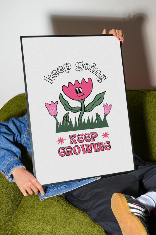 Siyah çerçeveli, beyaz zeminde pembe gülen çiçek, küçük çiçekler ve çimenler ile 'Keep Going' ve 'Keep Growing' yazılı motivasyon posteri.