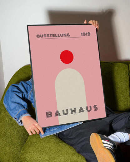 Pembe fon üzerinde kırmızı daire ve krem rengi kemer figürlü, 'Bauhaus 1919' yazılı minimalist poster.