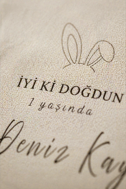 Kişiye özel bej doğum günü duvar örtüsü, tavşan kulaklı, 'İyi ki Doğdun 1 yaşında' yazılı.