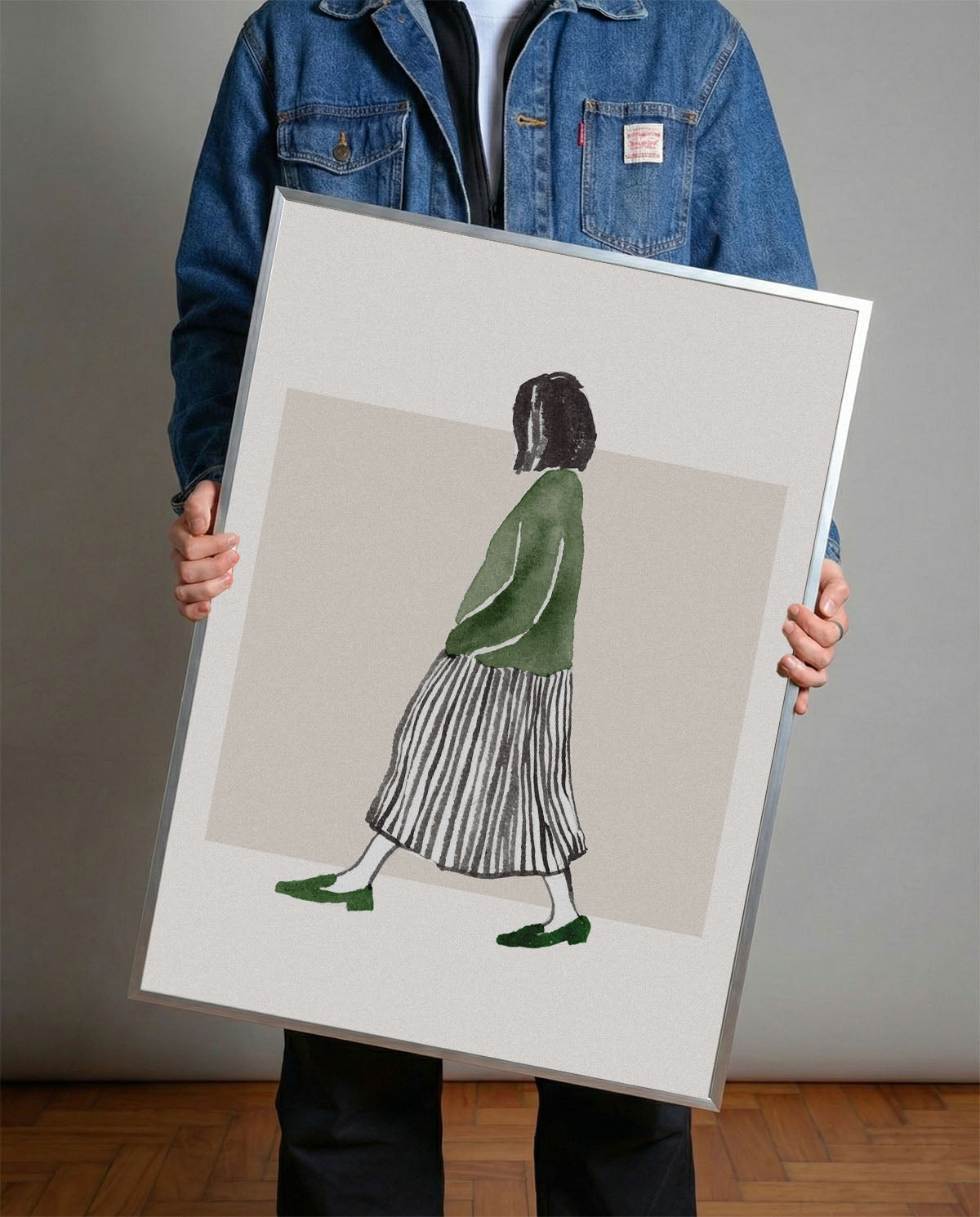 Minimalist suluboya tekniğiyle yapılmış, yeşil bluzlu ve çizgili etekli yürüyen kadın figürlü çerçeveli poster