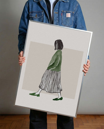 Minimalist suluboya tekniğiyle yapılmış, yeşil bluzlu ve çizgili etekli yürüyen kadın figürlü çerçeveli poster