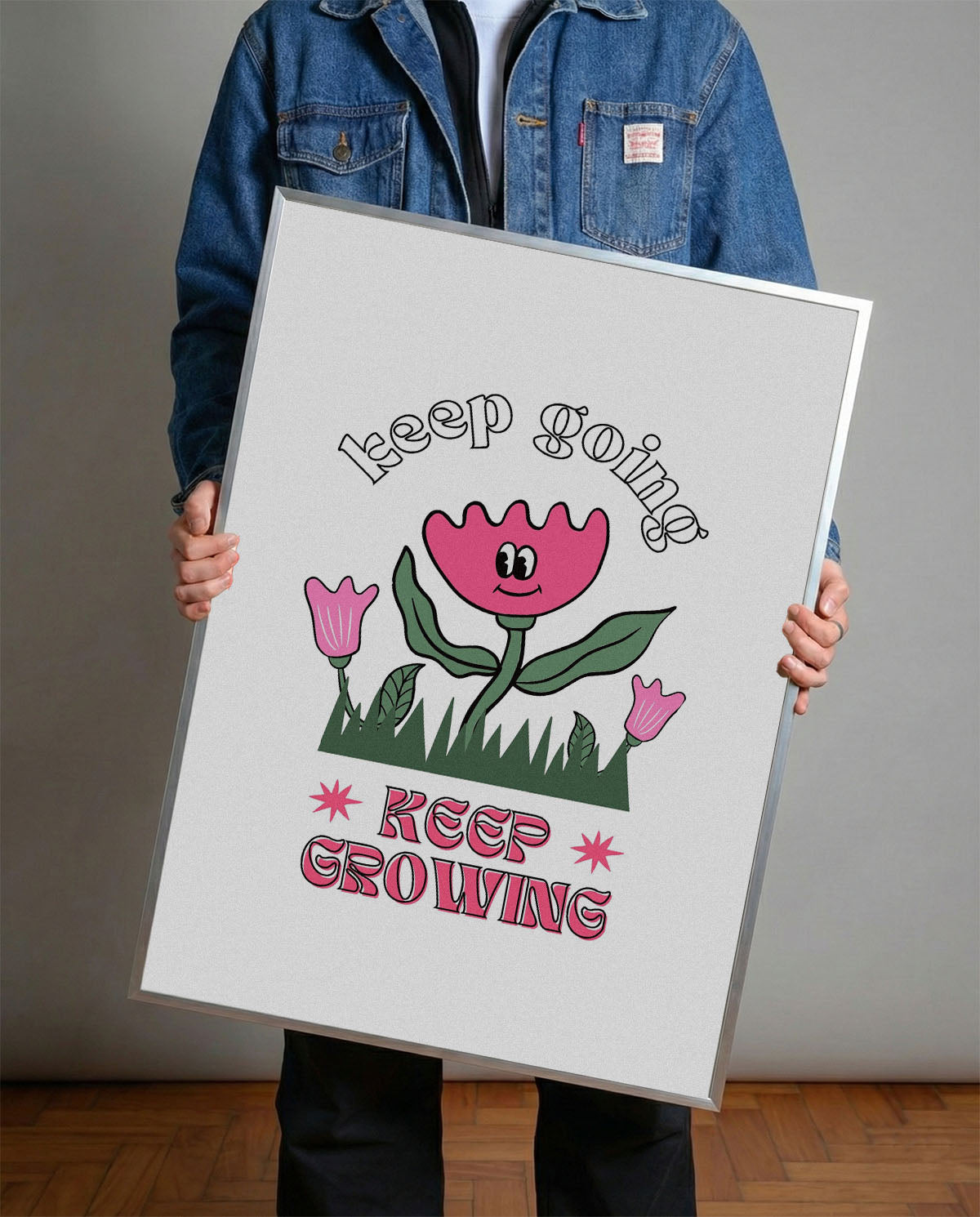 Siyah çerçeveli, beyaz zeminde pembe gülen çiçek, küçük çiçekler ve çimenler ile 'Keep Going' ve 'Keep Growing' yazılı motivasyon posteri.