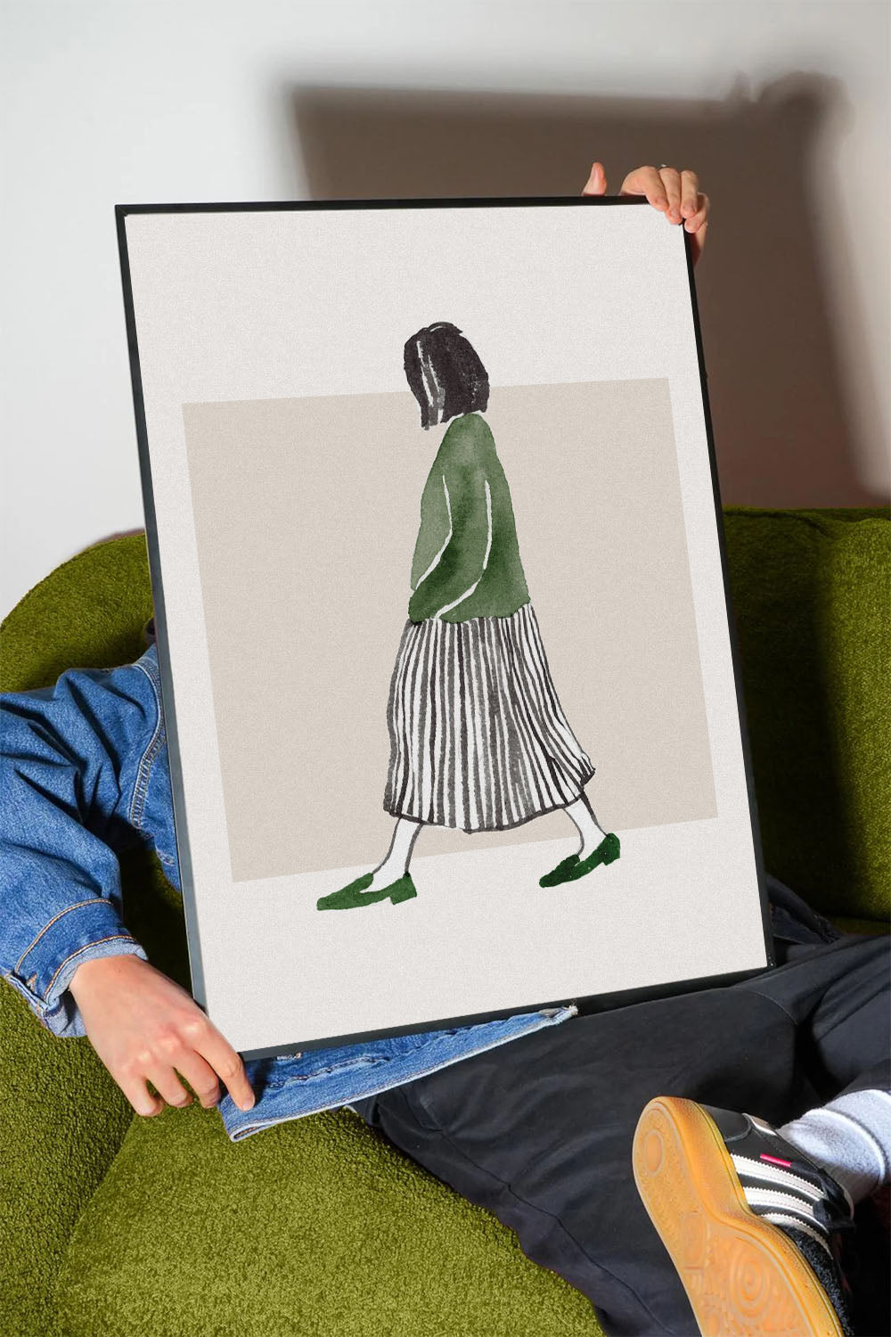 Minimalist suluboya tekniğiyle yapılmış, yeşil bluzlu ve çizgili etekli yürüyen kadın figürlü çerçeveli poster