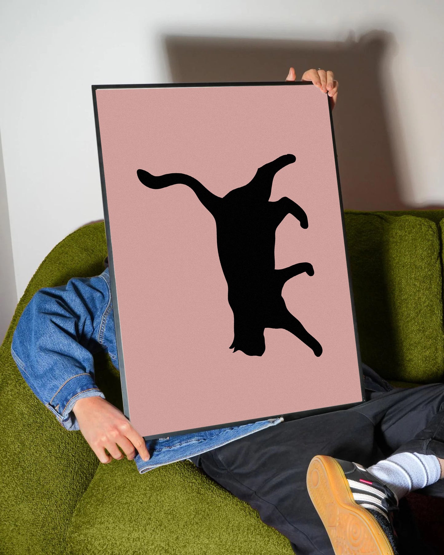 Siyah çerçeveli, pastel pembe fon üzerinde oyunbaz pozda siyah kedi silüeti minimalist poster.