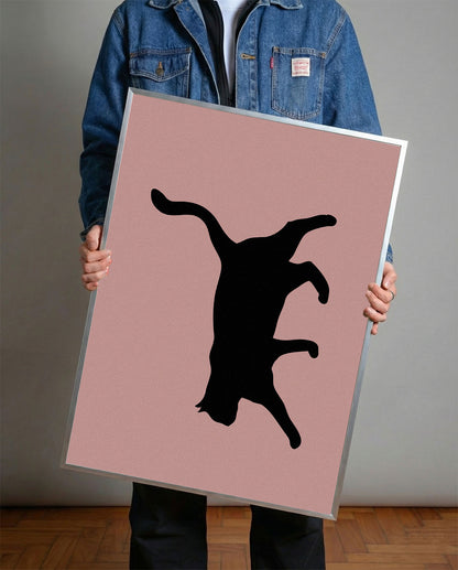 Siyah çerçeveli, pastel pembe fon üzerinde oyunbaz pozda siyah kedi silüeti minimalist poster.