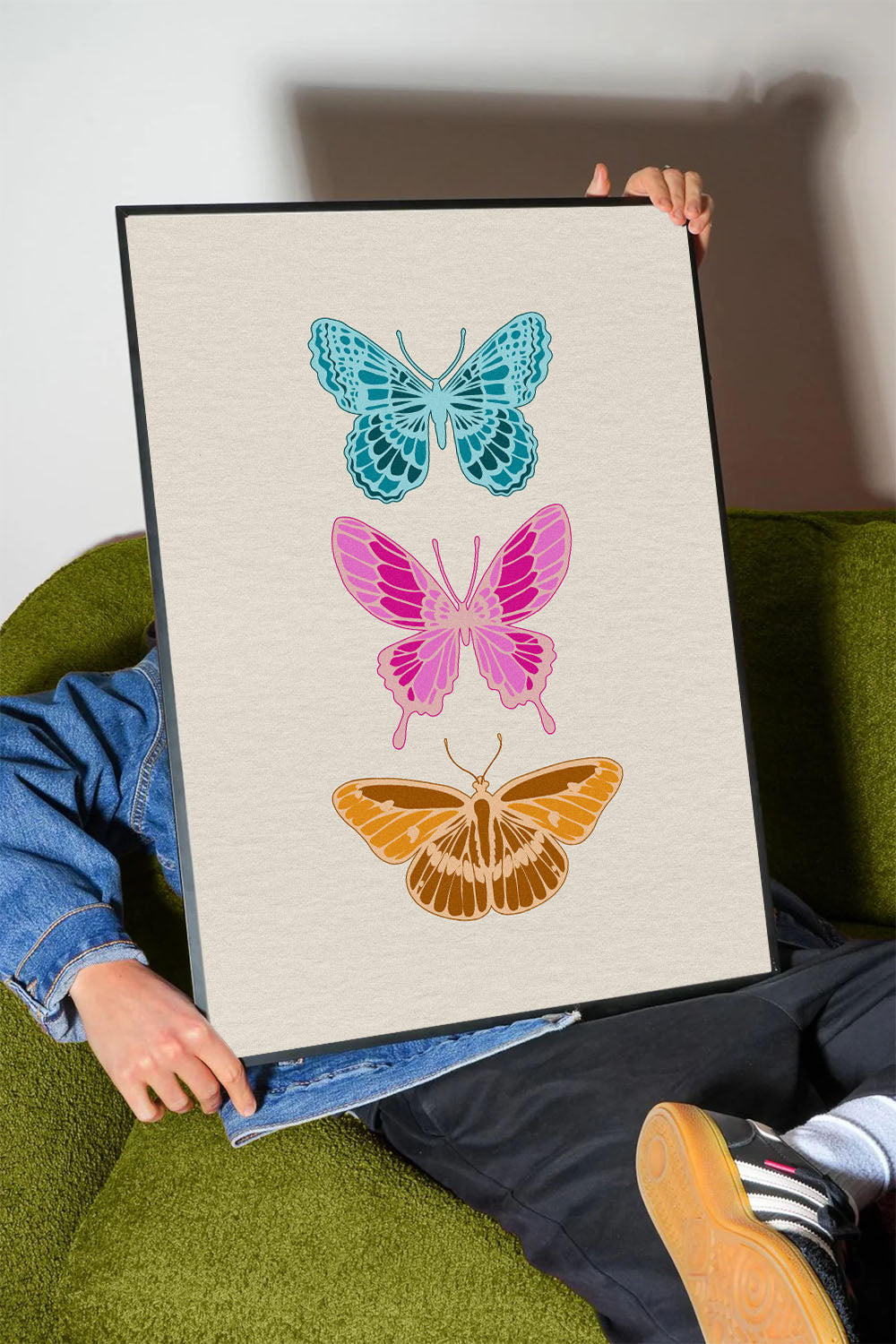 Siyah çerçeveli, açık renk dokulu zeminde mavi, pembe ve kahverengi üç modern kelebek desenli tablo.