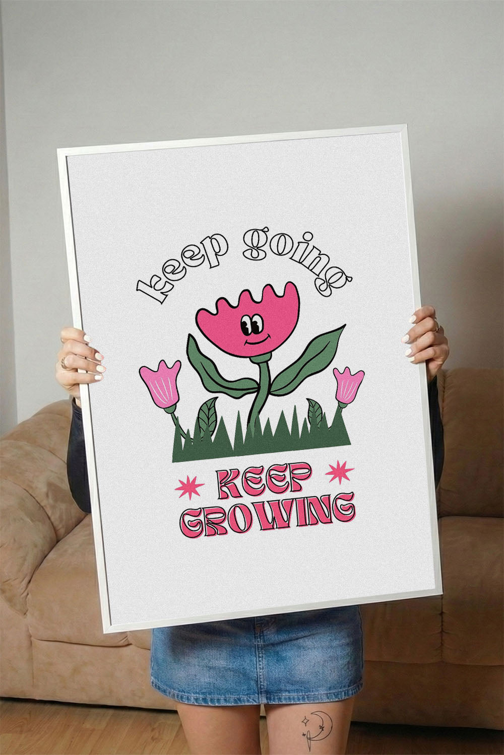Siyah çerçeveli, beyaz zeminde pembe gülen çiçek, küçük çiçekler ve çimenler ile 'Keep Going' ve 'Keep Growing' yazılı motivasyon posteri.